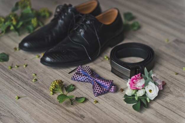 Elegant groom accessories including brooch, leather shoes, silk tie, and cufflinks arranged on marble surface