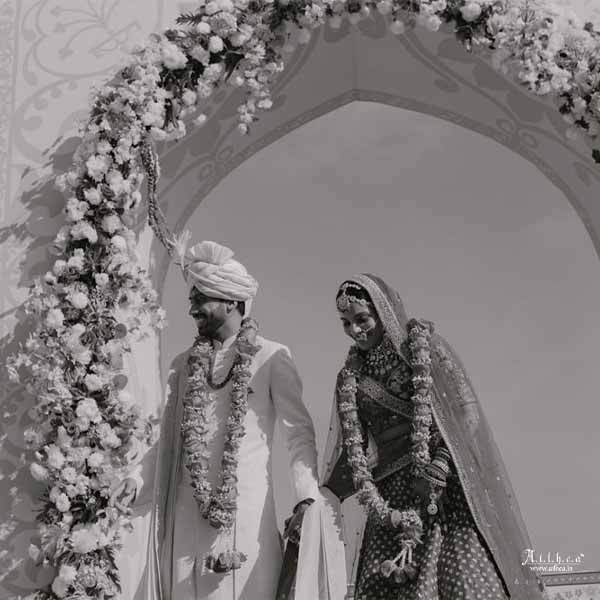 Bride and groom entering varmala ceremony under floral arch in classic black and white style
