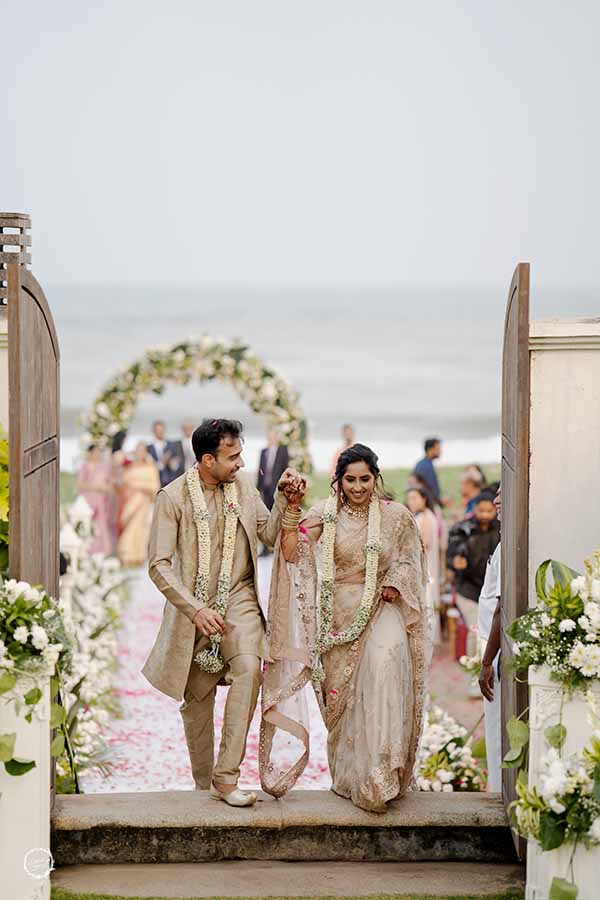 Bride and groom walking towards varmala stage at beach wedding ceremony